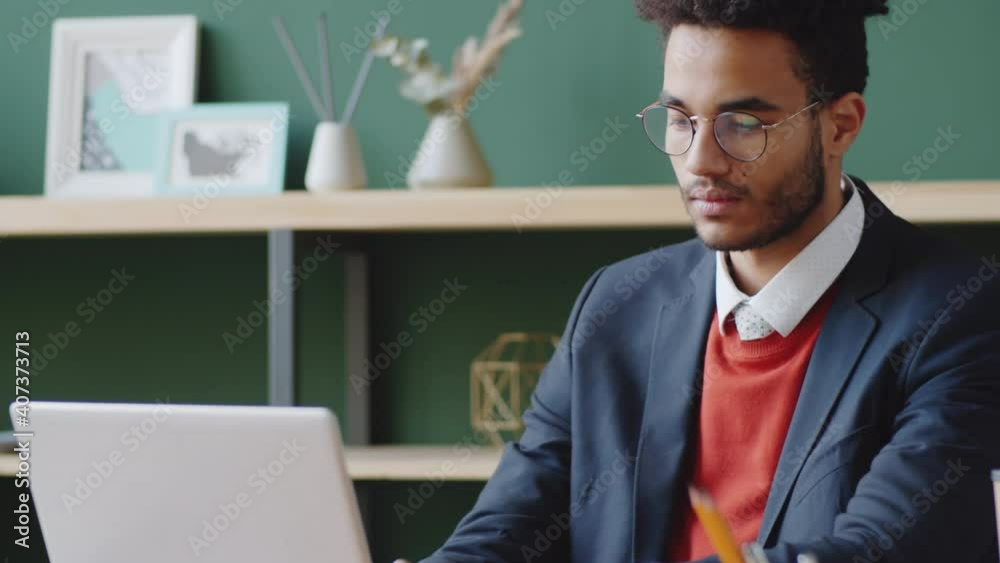 Young handsome businessman of mixed race ethnicity using laptop while working at desk in office with trendy interior Young handsome businessman of mixed race ethnicity using laptop while working at desk in office with trendy interior