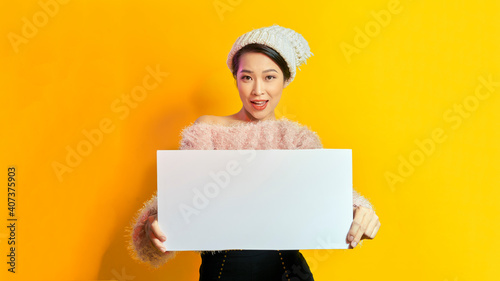 Business Concept - Close up Portrait young beautiful attractive Asian smiling showing plain white blank sign. Yellow Background.