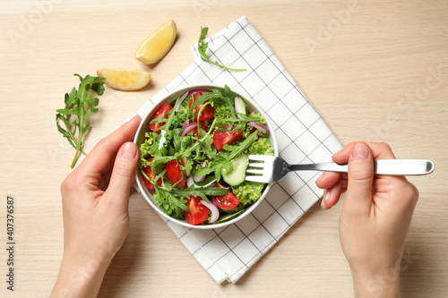 Woman eating delicious salad with arugula and vegetables at wooden table, top view