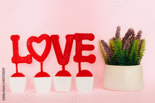 Red love word on the stand with heart shape and decorative plant isolated on pink background