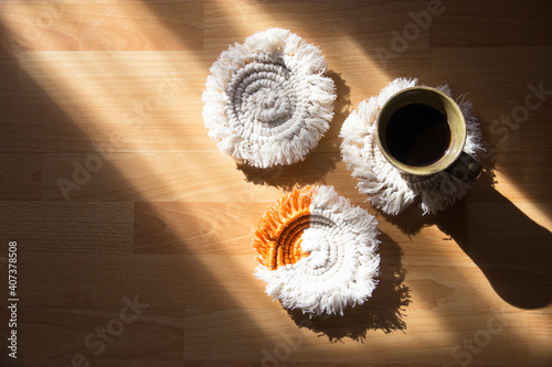 Macrame handmade Hobby.Top View black hot coffee in a cup on white macrame coasters with copy space.There was shadows that came from the window.
