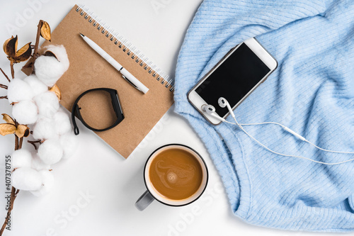 A modern creative background of a sweater, a cup of coffee, a smartphone and a branch of cotton. Cozy home working environment