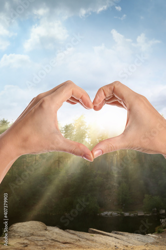 Woman making heart with hands outdoors on sunny day  closeup
