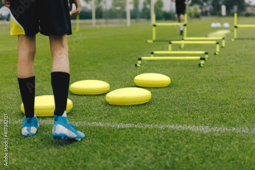 Soccer training equipment. Footballer ready to practice. Player is sportswear and soccer cleats. Sports training equipment: balance cushions, hurdles. Grass soccer field