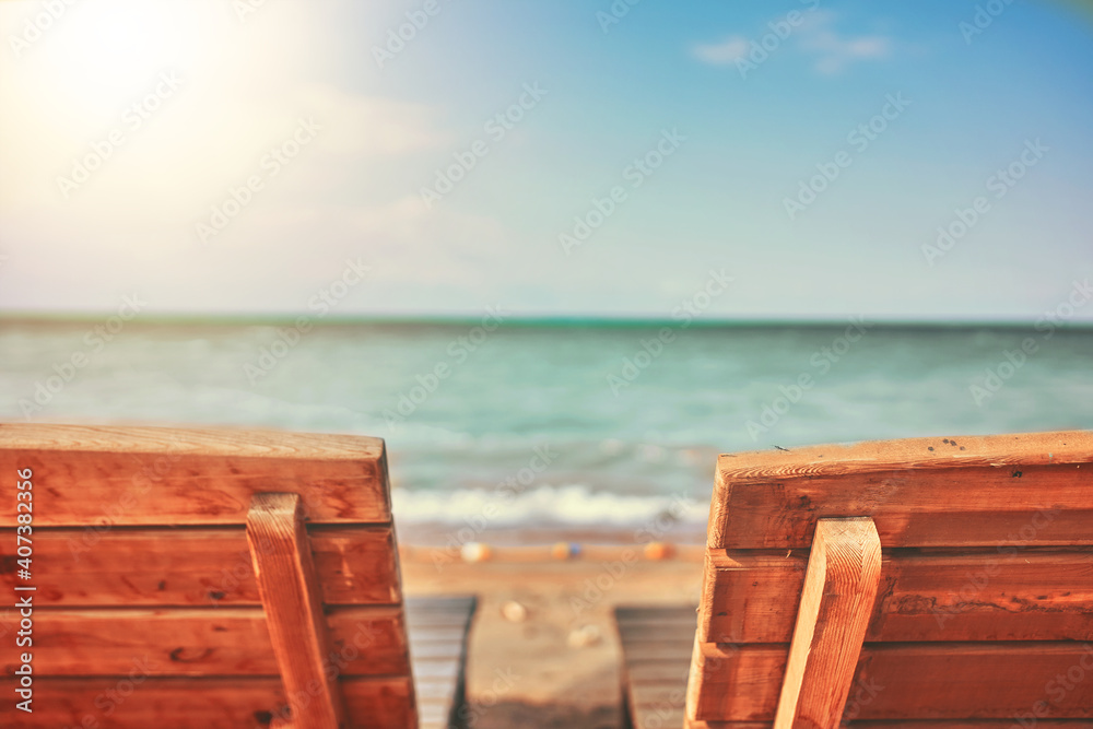 Two Wooden latticed sun beds. Beach at a boarding house or hotel. Sunbeds on the beach. Clear sea surface under a blue sky. Ocean in clear weather. 