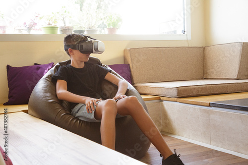 ragazzo adolescente gioca con la tecnologia virtuale grazie ad un visore nel salotto di casa photo