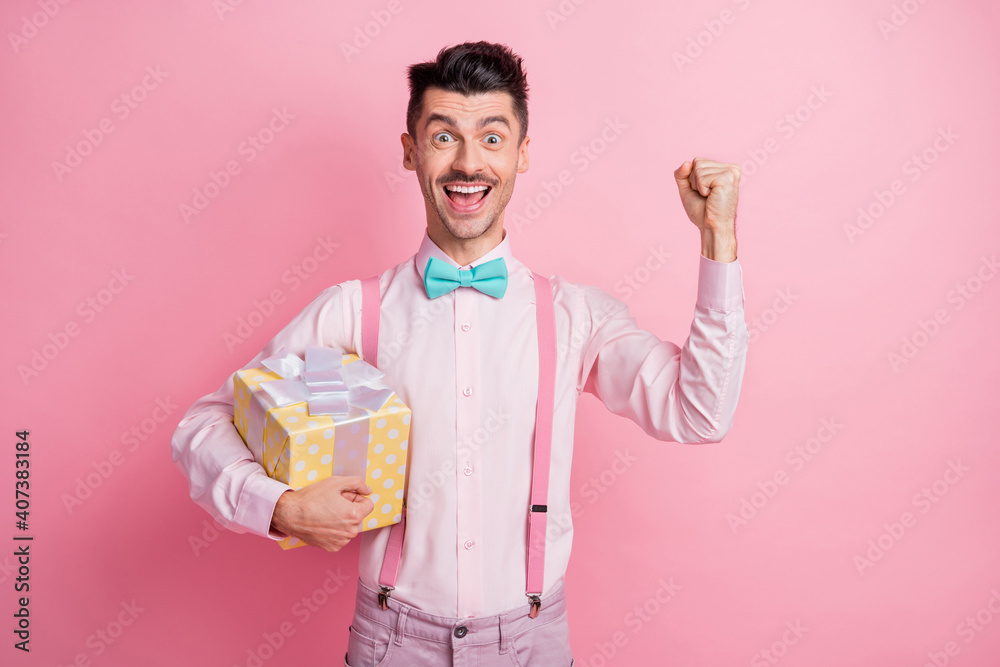 Photo portrait of cheerful man with raised fist holding gift box isolated on pastel pink colored background Photo portrait of cheerful man with raised fist holding gift box isolated on pastel pink colored background