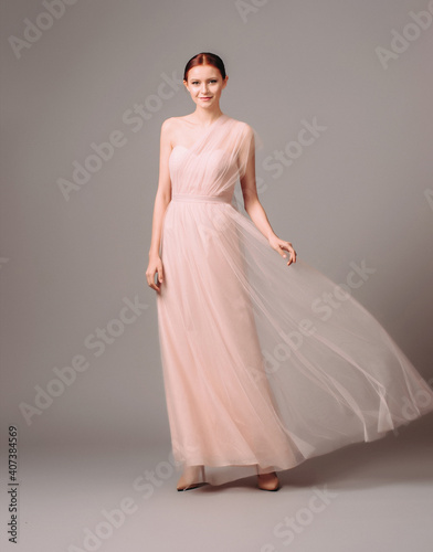 Bridesmaid's dresses. Elegant moscato dress. Beautiful pink chiffon evening gown. Studio portrait of young happy ginger woman. Transformer dress idea for an event.