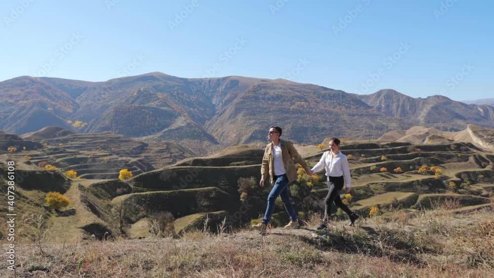 Young couple holding hands is walking on the background of mountain terraces on a sunny day. Young couple holding hands is walking on the background of mountain terraces on a sunny day.