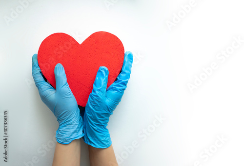 Hands in medical gloves holding a red heart shape model on white background.