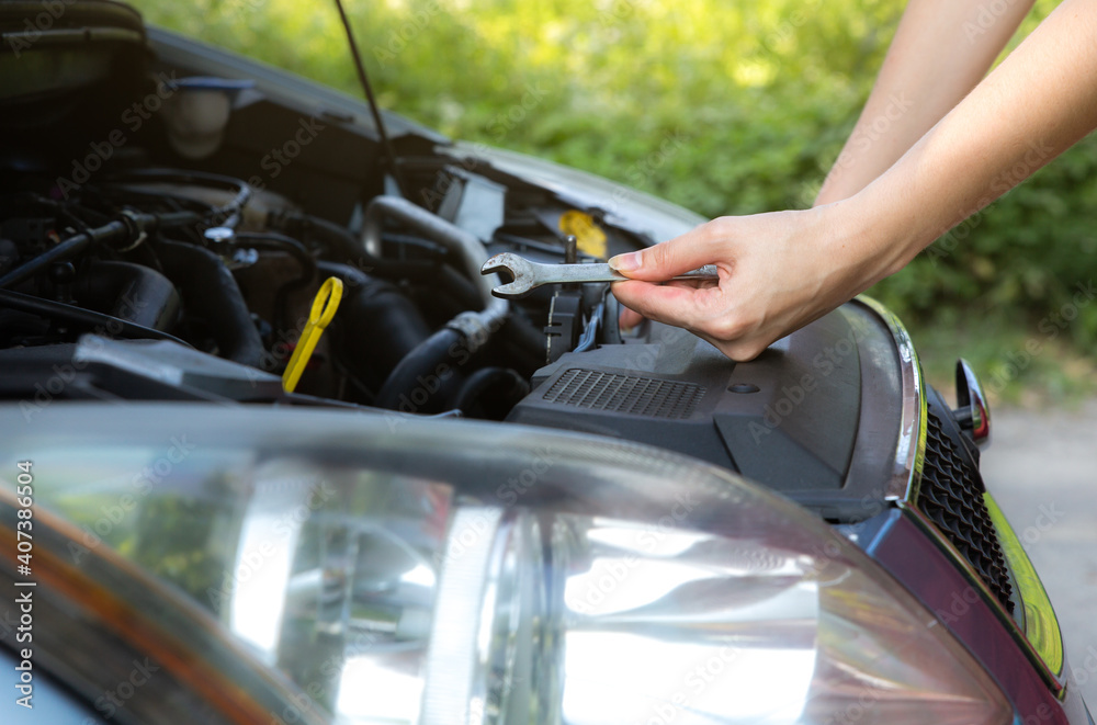 Woman is repairing broken car. Accident situation while travelling. Opened bonnet of vehicle. Girl is holding instruments for fixing. Woman is repairing broken car. Accident situation while travelling. Opened bonnet of vehicle. Girl is holding instruments for fixing.