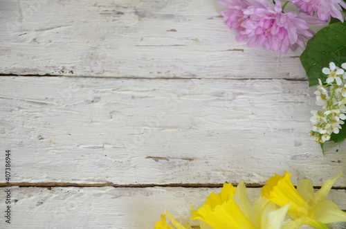 spring white and lilac or purple flowers on wooden white background and yellow daffodils. background for spring holidays. mother's day, easter