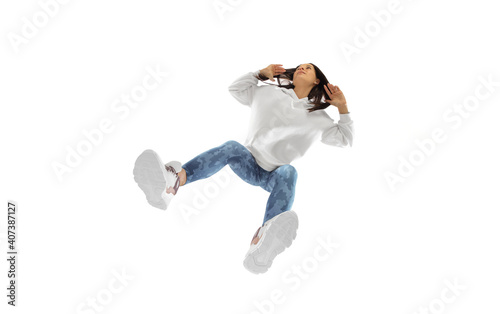 Moving. Young stylish woman in modern street style outfit isolated on white background, shot from the bottom. Caucasian fashionable model in shoes and overalls, musician, rapper performing.