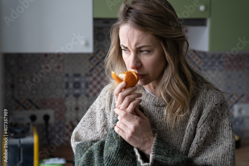Sick woman trying to sense smell of fresh tangerine orange, has symptoms of Covid-19, corona virus infection - loss of smell and taste, standing at home. One of the main signs of the disease.
