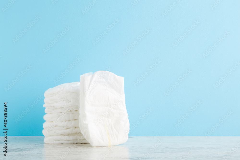 Stack of white soft new baby diapers on wooden table at light blue wall background. Pastel color. Closeup. Empty place for text or logo. Front view. - obrazy, fototapety, plakaty 