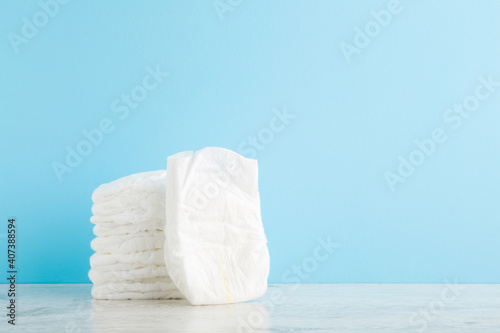Stack of white soft new baby diapers on wooden table at light blue wall background. Pastel color. Closeup. Empty place for text or logo. Front view. photo