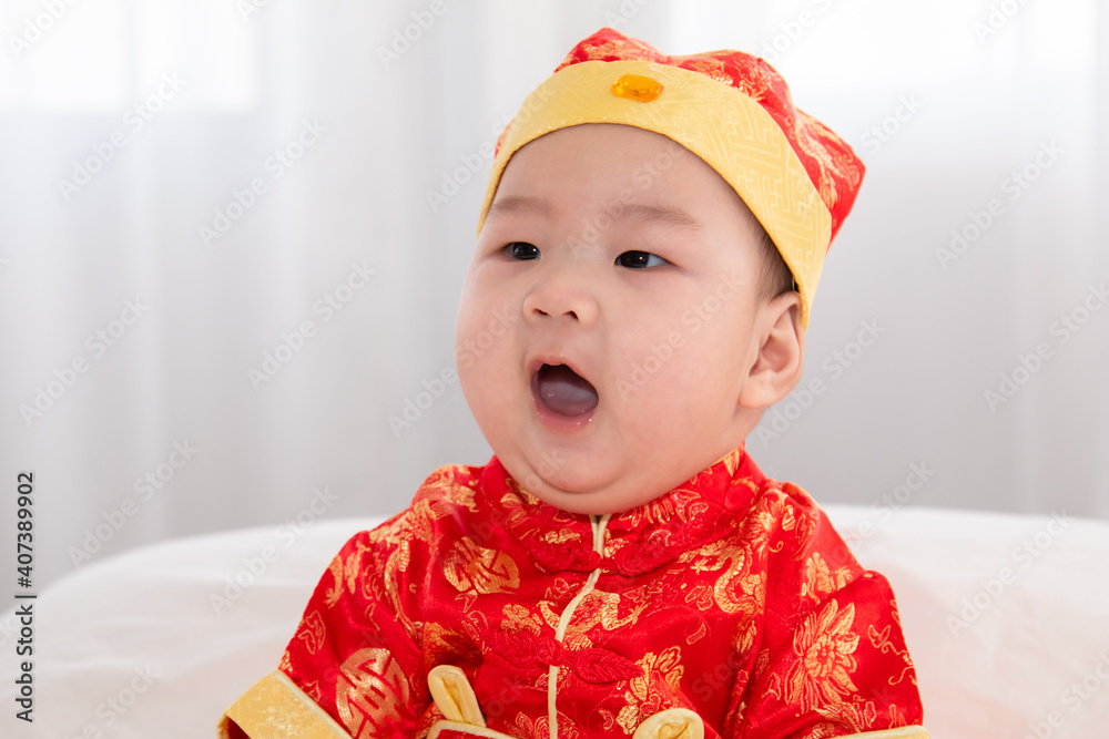 Adorable Asian boy in red Chinese Costume clothes sitting on bed at home looking for somethin with curiosity, innocent cute baby feel sleepy yawning boring waiting for mother feeding