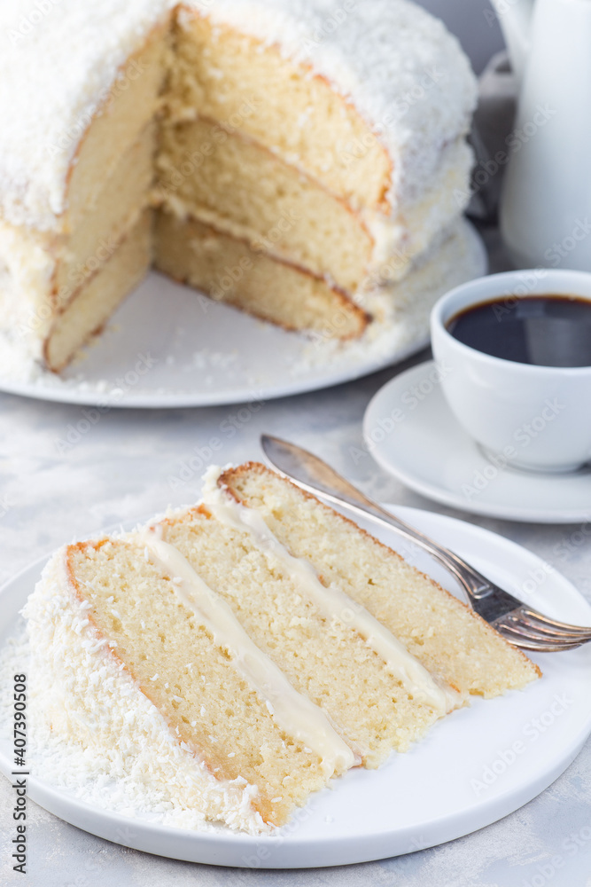 Piece of homemade coconut cake with cream cheese frosting and coconut flakes decoration, on white plate, vertical Piece of homemade coconut cake with cream cheese frosting and coconut flakes decoration, on white plate, vertical