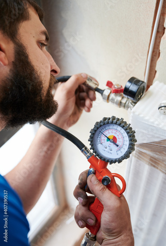 Close up of bearded man filling pipes with pressurized air to inspect for leaks in new installation. Worker using manometer, checking gas tightness of heating system. Concept of gas tightness testing. photo