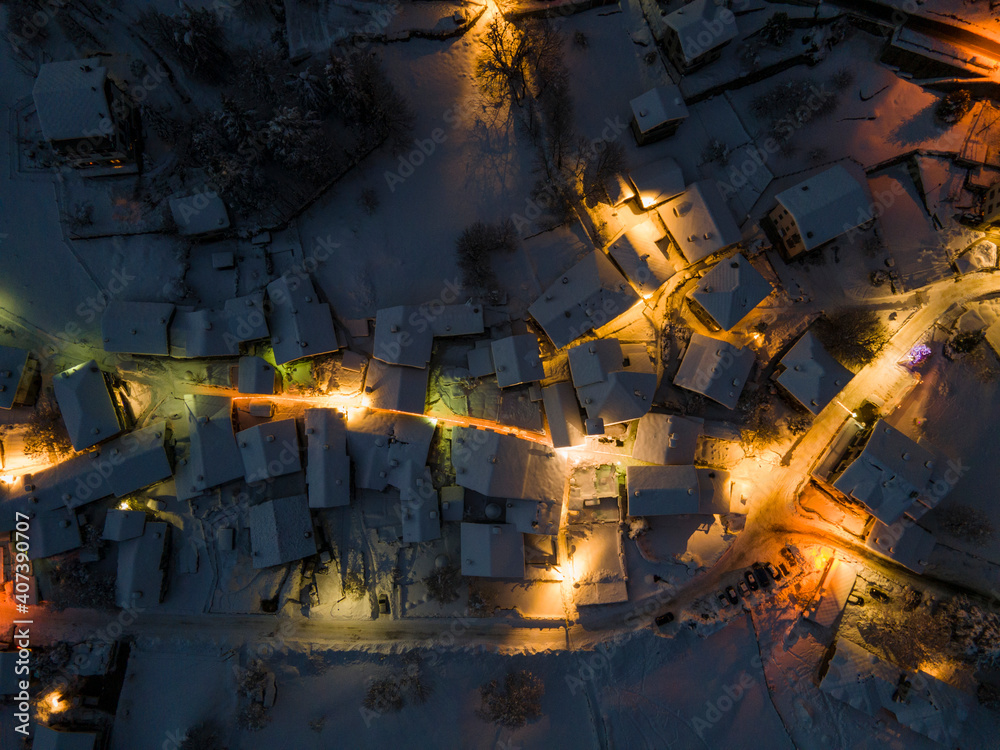 Aerial top down drone view of small town located in snowy mountain, Alps, Italy. Night long exposure with street lights.