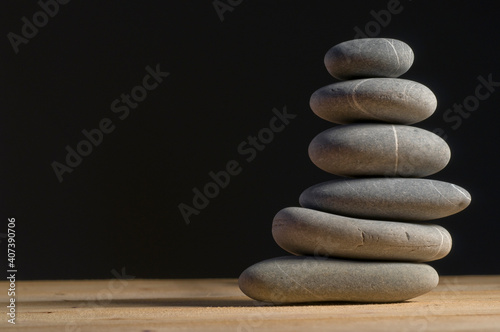 Balanced pile of six grey stones on wooden table  black background  equilibrium concept 
