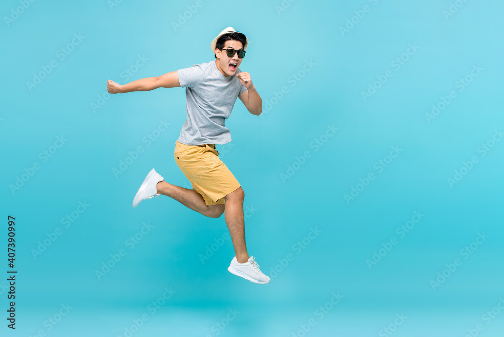 Energetic happy young Asian man jumping studio shot isolated in light blue background Energetic happy young Asian man jumping studio shot isolated in light blue background