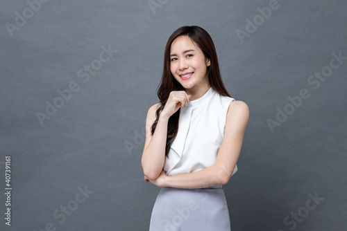 Portrait of smiling young beautiful Asian businesswoman looking at camera in isolated studio gray background