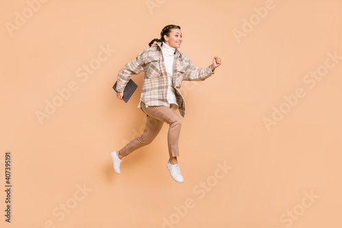 Full size profile photo of impressed girl jump hold laptop wear white shirt trousers sneakers isolated on beige color background