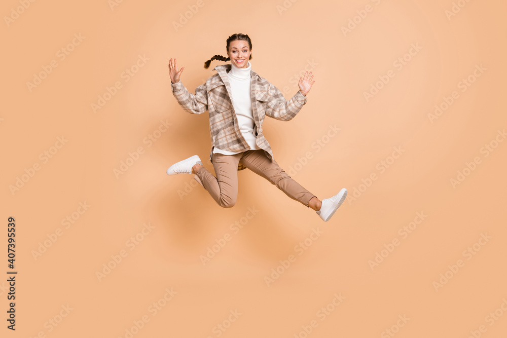 Full size photo of optimistic girl jump do kick wear white shirt trousers sneakers isolated on beige background Full size photo of optimistic girl jump do kick wear white shirt trousers sneakers isolated on beige background