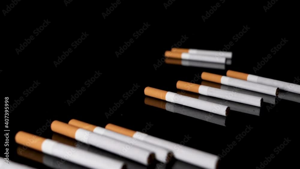 Pile of cigarettes are rolled out on a black mirroring surface in slow motion. Pile of cigarettes are rolled out on a black mirroring surface in slow motion.