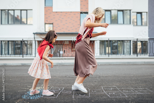 Cuadro en lienzo Side view of a joyful little girl playing hopscotch with her mother on playground outdoors