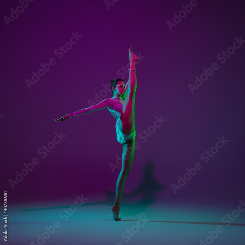 Going on. Young female athlete, rhythmic gymnastics artist dancing, training isolated on purple studio background in neon light. Beautiful girl practicing with equipment. Grace in performance.