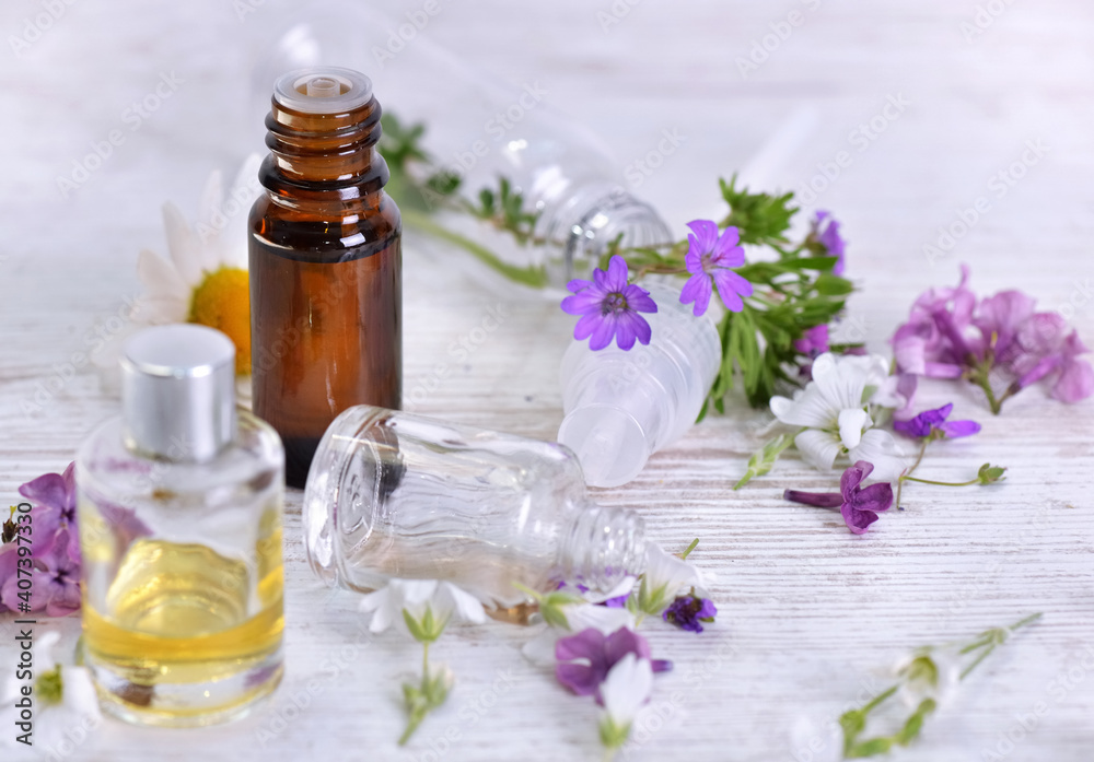 bottles of essential oil and colorful petals of fresh wild flowers on white table bottles of essential oil and colorful petals of fresh wild flowers on white table