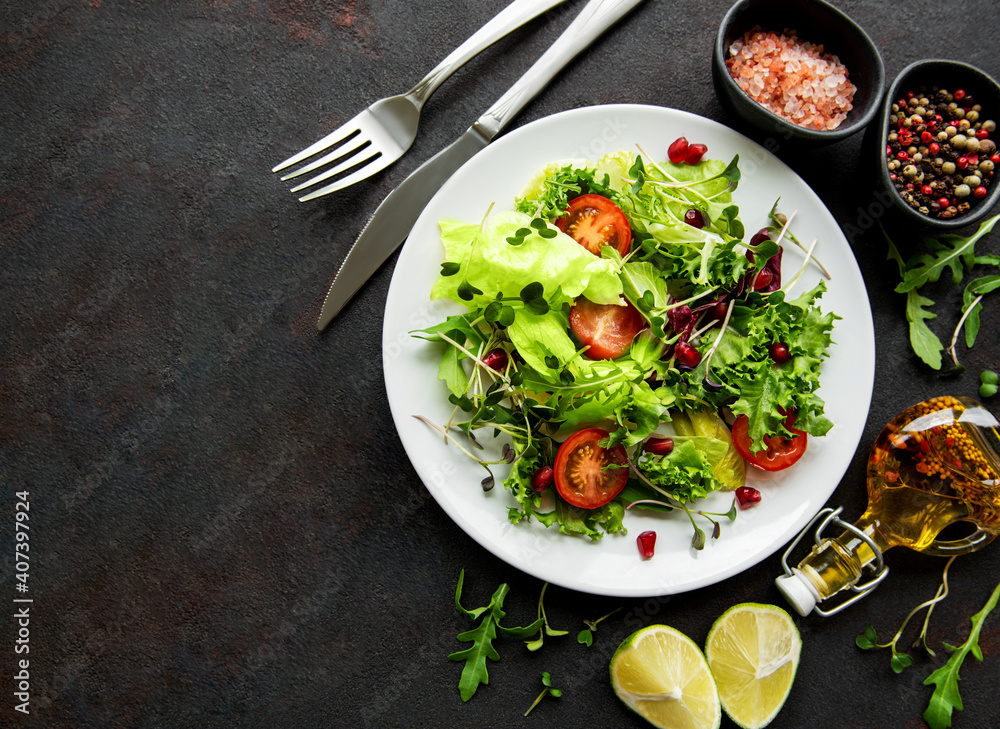 Fresh green mixed  salad bowl with tomatoes and microgreens  on black concrete background. Healthy food, top view.