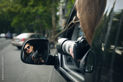 Private detective with camera spying from auto, view through car side mirror