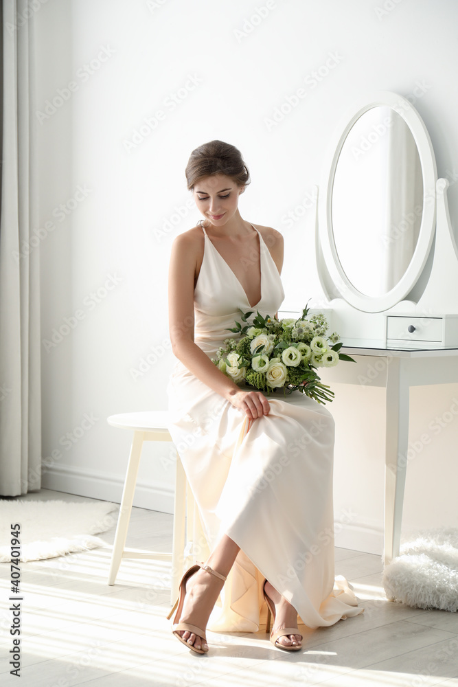 Young bride in wedding dress with beautiful bouquet near mirror indoors Young bride in wedding dress with beautiful bouquet near mirror indoors