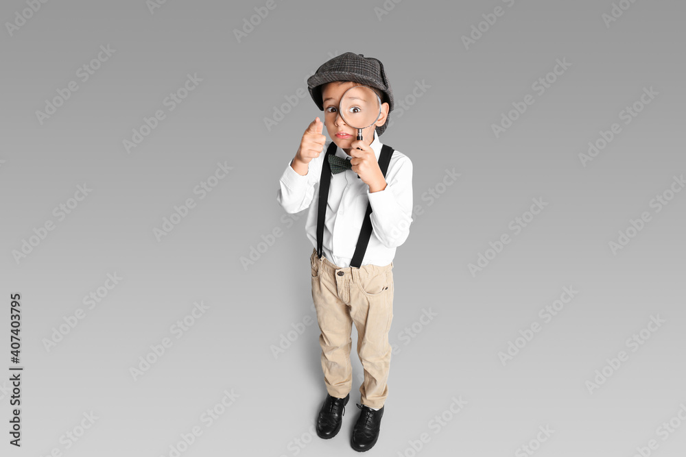 Little boy with magnifying glass playing detective on grey background Little boy with magnifying glass playing detective on grey background