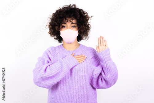 young beautiful caucasian woman wearing medical mask standing against white wall Swearing with hand on chest and open palm, making a loyalty promise oath © Roquillo