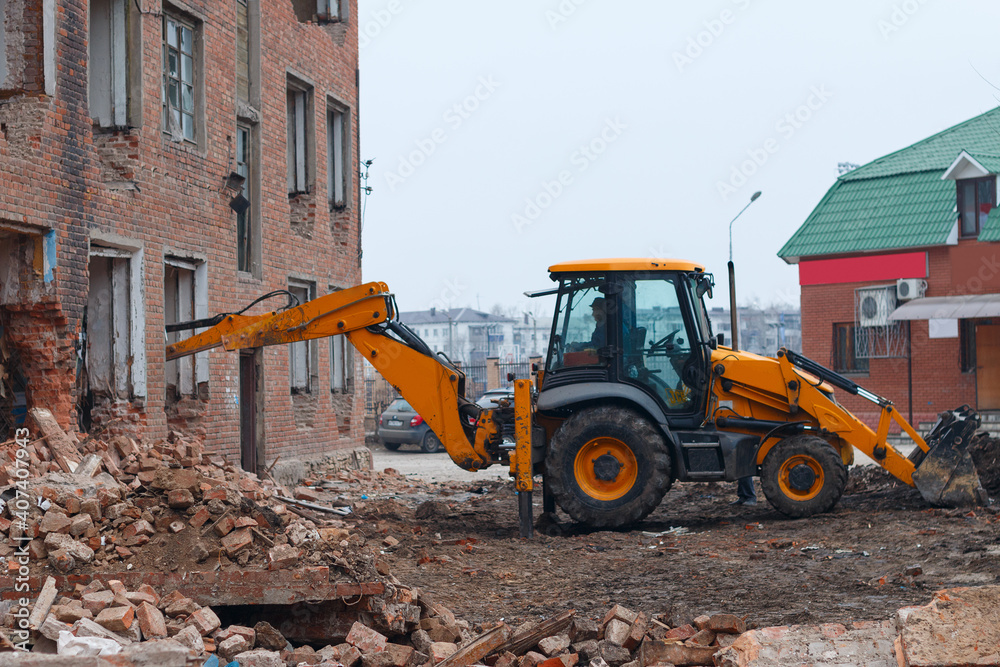 excavator disassembles the house, hydraulic bucket in the window of the building, work on dismantling old houses
