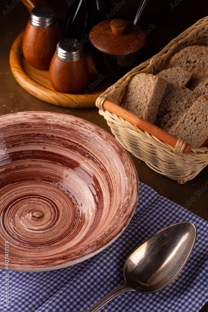 Empty ceramic plate, spice containers and bread in a basket Empty ceramic plate, spice containers and bread in a basket