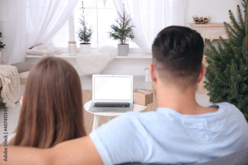 Couple using video chat on laptop in room decorated for Christmas Couple using video chat on laptop in room decorated for Christmas