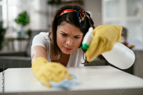 Tired woman cleaning home. Portrait of young woman looking tired while cleaning a desk in living room.