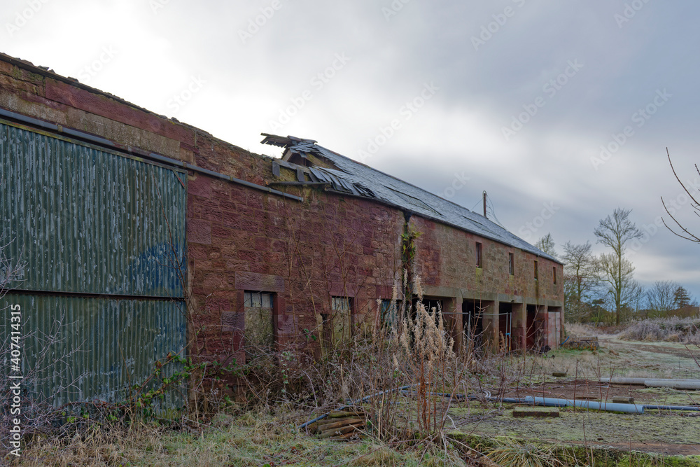 A ruined stone Farm Barn with the slate Roof fallen in, and bits of equipment lying on the hardstanding next to the machinery sheds. A ruined stone Farm Barn with the slate Roof fallen in, and bits of equipment lying on the hardstanding next to the machinery sheds.