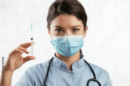 Beautiful female doctor with medical mask. Portrait of nurse with syringe in her hand