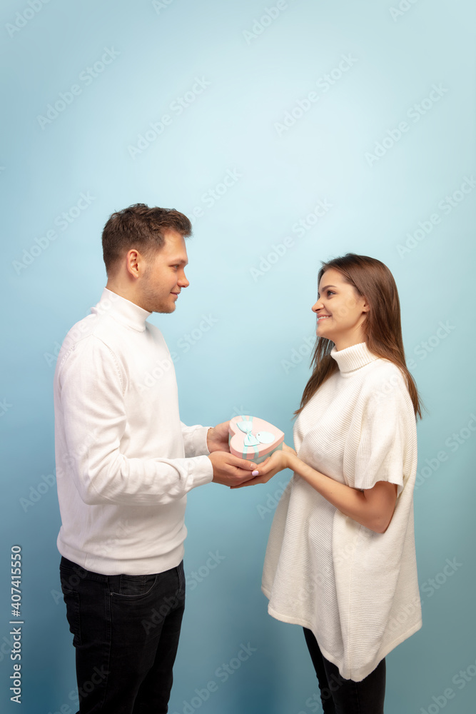 White heart. Beautiful couple in love on blue studio background. Saint Valentine's Day, love, relationship and human emotions concept. Copyspace. Young man and woman look happy together. White heart. Beautiful couple in love on blue studio background. Saint Valentine's Day, love, relationship and human emotions concept. Copyspace. Young man and woman look happy together.