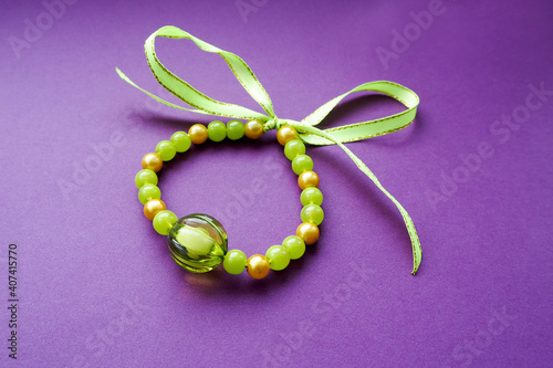 women's bracelet from green beads of different sizes tied with satin ribbon lies on a lilac background side view