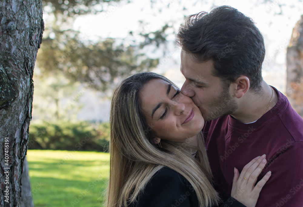 Lovers Kissing Outdoors In The Park. Happy Lovers By A Park. In Love Lovers Kissing Outdoors In The Park. Happy Lovers By A Park. In Love