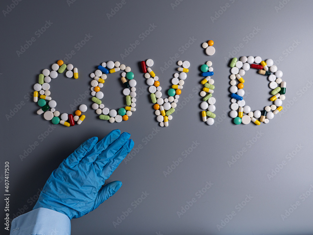 Hand in blue medical protective glove show stop gesture and sign COVID made of pills, tablets and capsules on gray table
