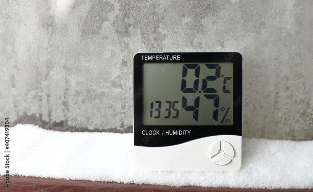 Digital thermometer on a window with snow on the background of frozen glass. Electronic thermometer and hygrometer for temperature and humidity control