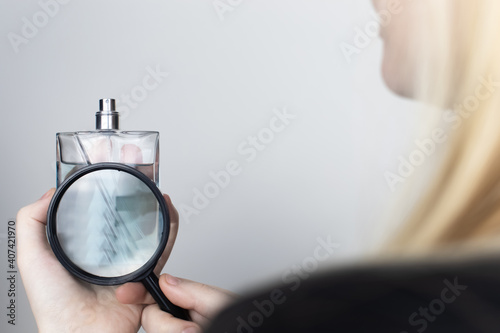 A woman examines the harmful ingredients of the perfume through a magnifying glass. Place for your text. The concept of hazardous substances in cosmetics and household chemicals photo